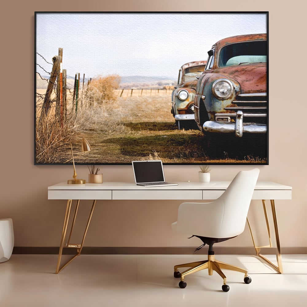 Tablou canvas cu doua masini ruginite pe un camp uscat, in rama de aluminiu negru, pe perete intr-un birou